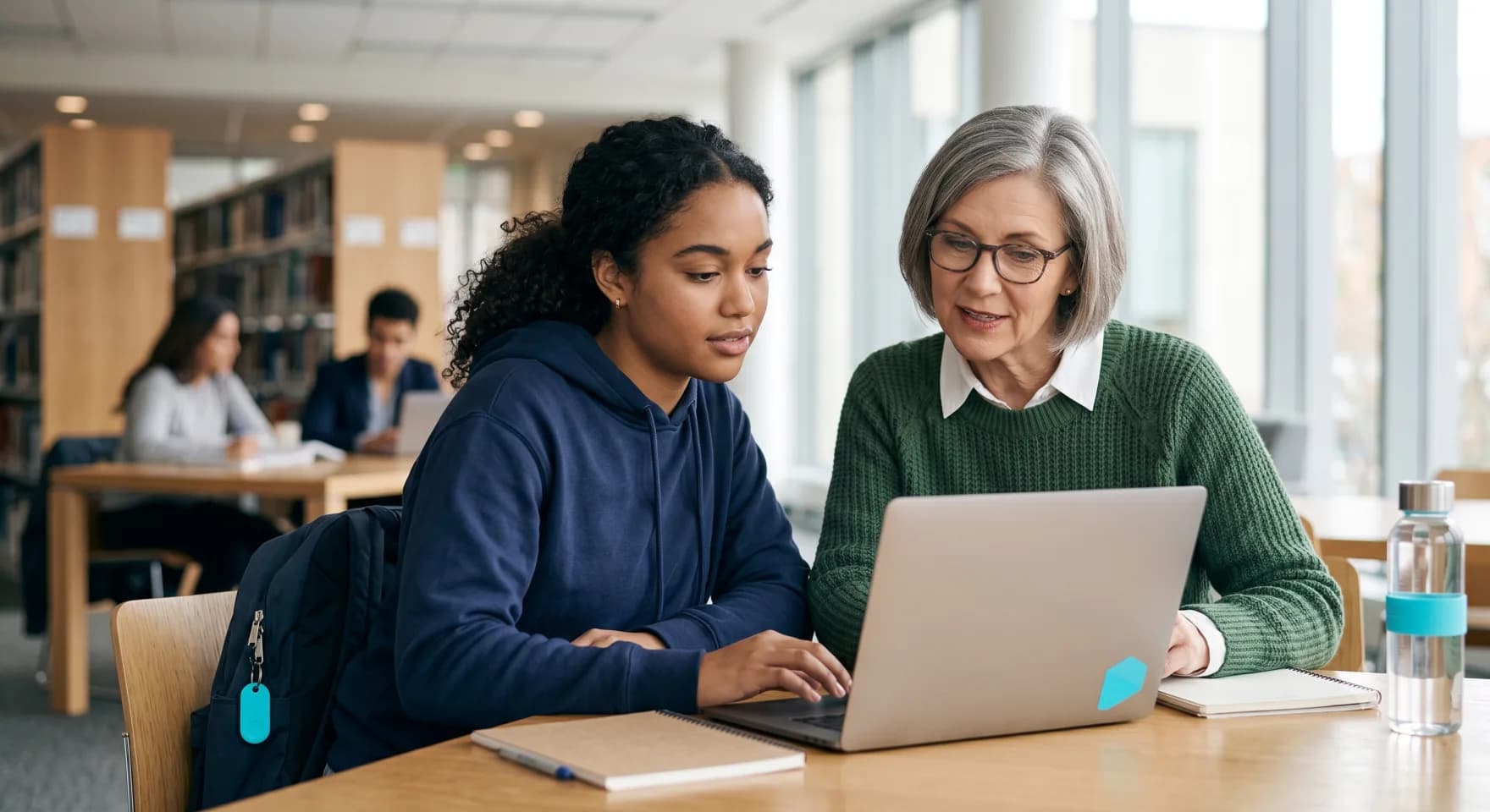 A student and a faculty member reviewing assessment results together on a laptop in a university library